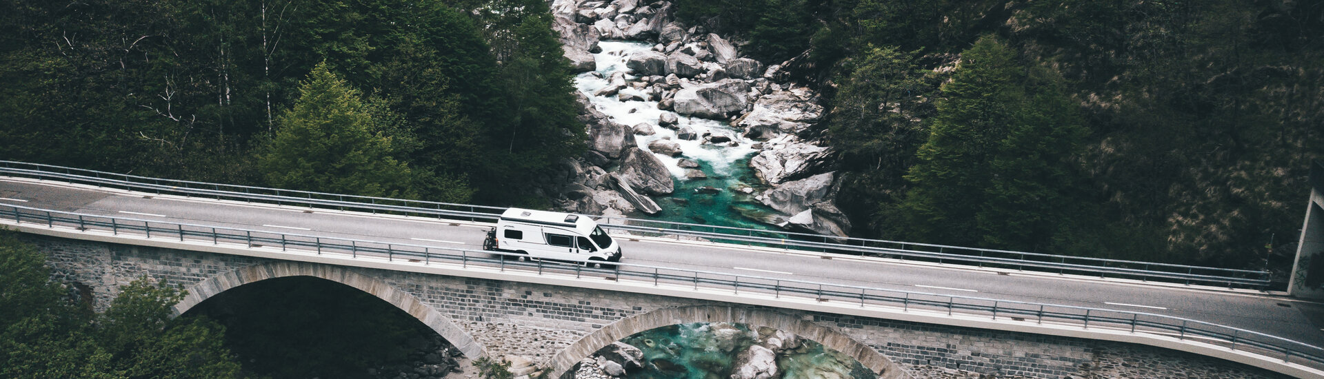 Camper unterwegs über eine Steinbrücke an einem Gebirgsbach
